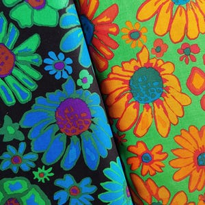 May include: Two fabric swatches with large floral patterns. One features green, blue, and purple flowers on a black background. The other has orange and yellow flowers on a green background. The flowers have blue centers.