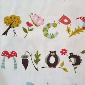 Könnte beinhalten: Weißer Stoff mit einem sich wiederholenden Muster von Waldtieren und -elementen. Das Design umfasst einen Baum, einen Schmetterling, eine Raupe, einen Zwerg, einen Fuchs, eine Eule, einen Igel, einen Waschbären und Pilze in verschiedenen Farben. Der Stoff ist aus Bio-Baumwolle.