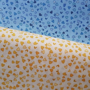 May include: Two fabric swatches with a pattern of small hearts. The top swatch is a light blue with dark blue hearts. The bottom swatch is white with yellow hearts.