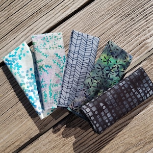 Peut inclure: Cinq échantillons de tissu avec des motifs différents dans des tons de bleu, vert et noir. Les échantillons sont disposés en éventail sur une surface en bois.