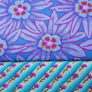 May include: Two fabric patterns. The top fabric shows large, stylised blue flowers with purple outlines and orange centres on a light blue background. The bottom fabric has diagonal stripes of blue and white with purple floral sprigs.