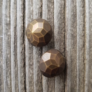 Peut inclure: Deux clous décoratifs ronds en laiton facetté sur une surface en bois.