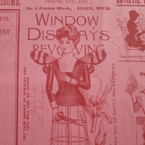 Könnte beinhalten: Eine Vintage-Werbung für einen drehbaren Schaufensterständer. Die Anzeige zeigt eine Frau mit Flügeln, die eine Schere vor einem Ständer mit einer käfigartigen Struktur hält. Der Text lautet "Window Displays Revolving" und "Manufactured to Order". Die Anzeige ist in Rot auf rosa Hintergrund gedruckt.