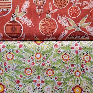 May include: Red fabric with a repeating pattern of stylized Christmas ornaments. The ornaments are in shades of orange, red, and brown. The background is a solid red. The fabric is folded in half, revealing a second fabric with a green and white floral pattern.