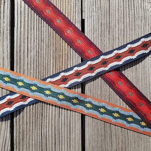 Può includere: Tre cinturini in tessuto intrecciato con motivi geometrici in rosso, blu, bianco e arancione. I cinturini sono incrociati l'uno sull'altro su una superficie di legno.