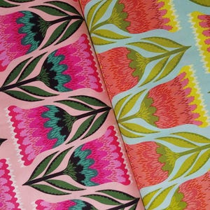 Può includere: Due campioni di tessuto con motivi floreali. Uno presenta fiori rosa con accenti turchese e neri su sfondo rosa chiaro. L'altro ha fiori arancioni e gialli con foglie verdi su sfondo azzurro.