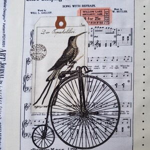 Op de afbeelding: Cr&egrave;mekleurige stof met een vintage ontwerp. Het toont bladmuziek, een kolibrie op een hoge bi en de tekst "She's Sleeping on the Old Missouri Shore." Bevat een kaartje van Willow Lake Amusement Park.