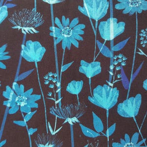 Può includere: Un tessuto con un motivo floreale con fiori e foglie turchesi stilizzati su uno sfondo marrone scuro. Il design include varie forme e dimensioni di fiori, con lunghi steli e foglie.