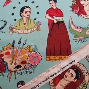 May include: Light blue fabric featuring Frida Kahlo-inspired illustrations in a tattoo style. The design includes portraits, paint palettes, flowers, and text such as "MI VIDA" and "FRIDA". A strip of fabric with text is visible.