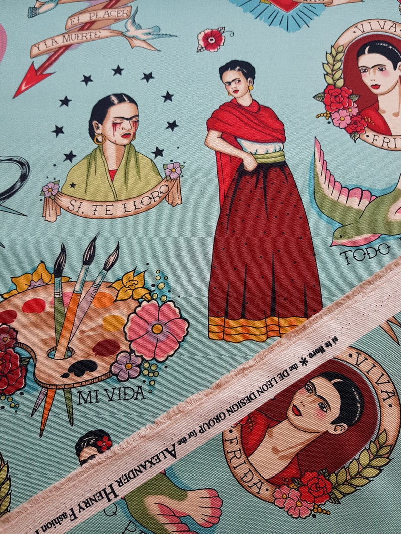 May include: Light blue fabric featuring Frida Kahlo-inspired illustrations in a tattoo style. The design includes portraits, paint palettes, flowers, and text such as "MI VIDA" and "FRIDA". A strip of fabric with text is visible.