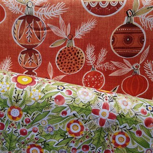 May include: Two fabric swatches with a Christmas theme. The top swatch is red with a white pattern of stylized Christmas ornaments and pine branches. The bottom swatch is white with a green pattern of stylized flowers and berries.