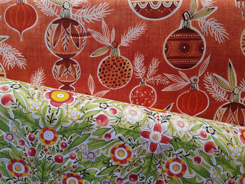 May include: Two fabric swatches with a Christmas theme. The top swatch is red with a white pattern of stylized Christmas ornaments and pine branches. The bottom swatch is white with a green pattern of stylized flowers and berries.