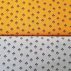 Pode incluir: Duas amostras de tecido com um padrão repetido de trevos pretos. A amostra superior é de cor laranja brilhante e a amostra inferior é de cor cinza claro.