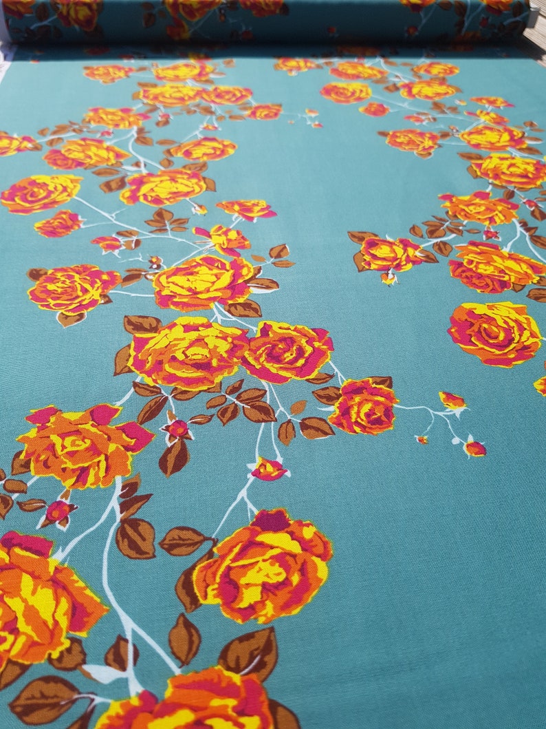 May include: Teal fabric with a floral pattern of orange and yellow roses with pink centers. The roses are arranged in a vine-like pattern.