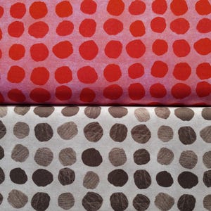 May include: Two fabric samples, one above the other. The top fabric is a light red with large, evenly spaced, red polka dots. The bottom fabric is off-white with large, evenly spaced, brown polka dots.