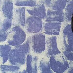 May include: A blue fabric background with a white paint splatter pattern. A black pen is lying on the fabric.