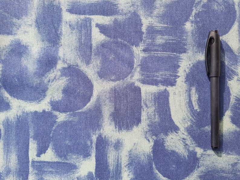 May include: A blue fabric background with a white paint splatter pattern. A black pen is lying on the fabric.