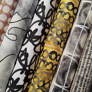 May include: Five fabric samples rolled up, showcasing different patterns. The patterns include black and white abstract designs, a yellow and black geometric pattern, a black and white grid pattern, and a brown and white polka dot pattern.