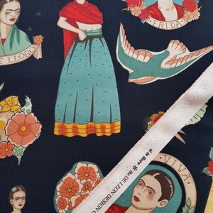Op de afbeelding: Een donkerblauwe stof met een herhalend patroon van Frida Kahlo-afbeeldingen, bloemen en een duif. De stof heeft de tekst "FRIDA" en "VIVA."