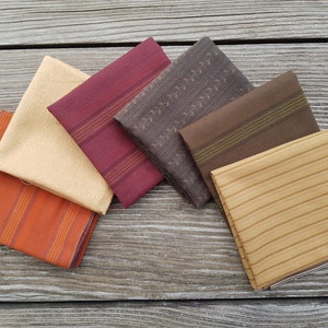 Peut inclure: Cinq échantillons de tissu dans différentes nuances de brun, orange et beige. Les échantillons présentent différents motifs, notamment des rayures, de petits motifs floraux et un motif texturé.