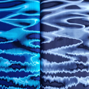 Könnte beinhalten: Zwei Stoffmuster mit einem blauen und weißen Wasserwellenmuster. Der Stoff links ist ein dunkleres Blau mit einem lebendigeren blauen Wellenmuster. Der Stoff rechts ist ein helleres Blau mit einem subtileren Wellenmuster.