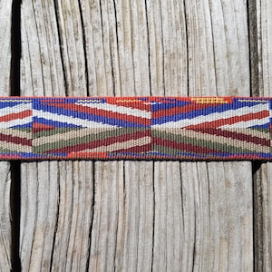 Op de afbeelding: Een close-up van een geweven lint met een rood, blauw, wit, groen en bruin patroon. Het lint ligt op een houten oppervlak.