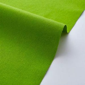 Könnte beinhalten: Nahaufnahme eines leuchtend grünen Stoffes mit strukturierter Oberfläche. Der Stoff ist gefaltet, wodurch Schatten entstehen und die Textur des Materials hervorgehoben wird. Die leuchtend grüne Farbe dominiert das Bild und deutet auf ein Textil- oder Bastelmaterial hin.
