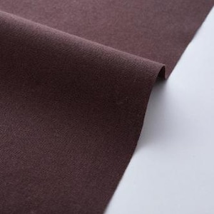 May include: Close-up of a folded piece of dark brown fabric. The fabric has a soft texture and a slight sheen. The folds create shadows and highlights, emphasizing the material's depth and texture. The fabric is set against a white background.