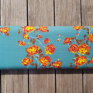 May include: Teal fabric with a floral pattern of orange and pink roses. The roses are arranged in a repeating pattern on the fabric.