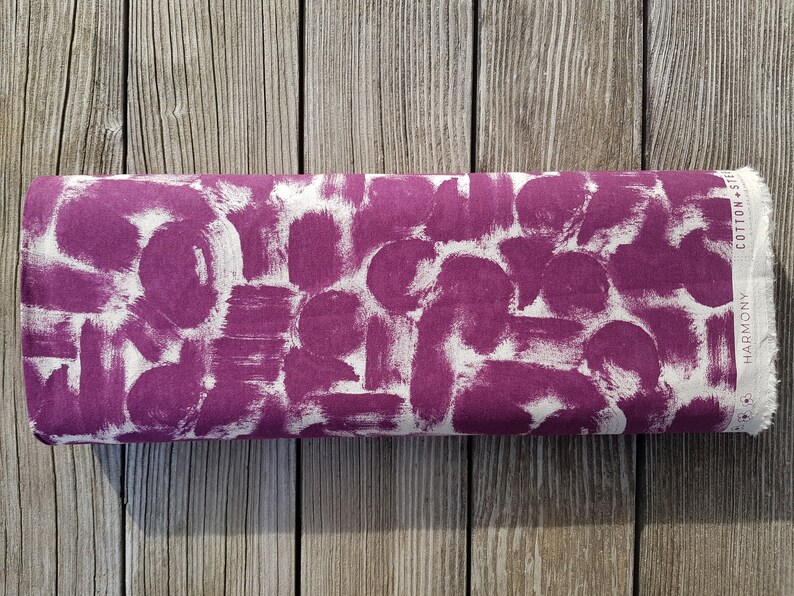 May include: A close-up of a purple fabric with a white abstract pattern. The fabric has the words "HARMONY" and "COTTON + SILK" printed on the edge.