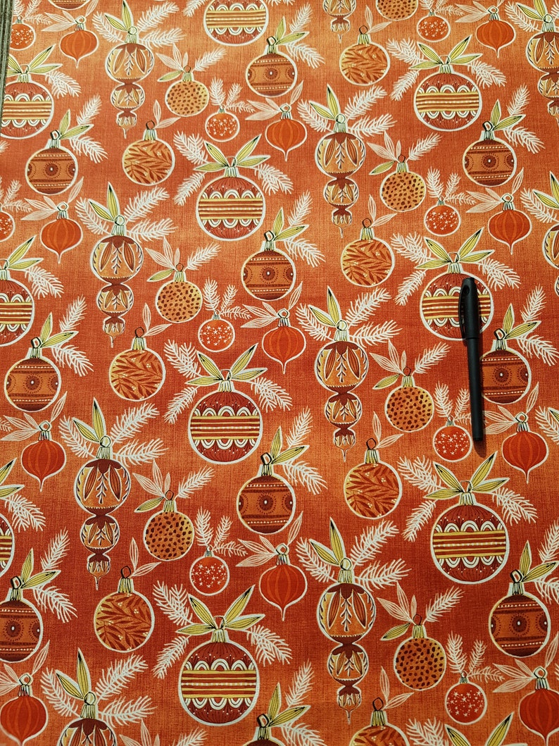 May include: Orange fabric with a repeating pattern of stylized Christmas ornaments. The ornaments are in shades of brown, orange, and white. The background is a textured orange.