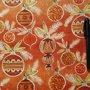 May include: A red fabric with a repeating pattern of stylized Christmas ornaments. The ornaments are in shades of brown, orange, and yellow with white outlines. The fabric has a subtle texture.
