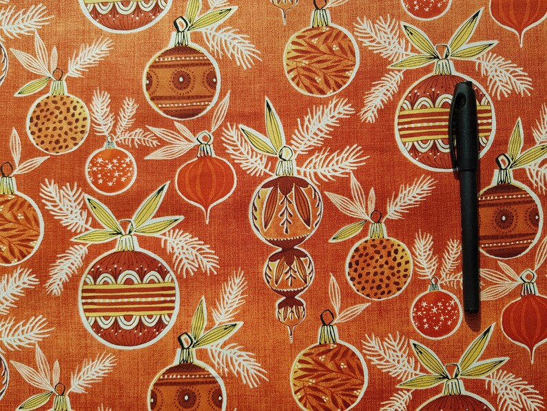 May include: A red fabric with a repeating pattern of stylized Christmas ornaments. The ornaments are in shades of brown, orange, and yellow with white outlines. The fabric has a subtle texture.