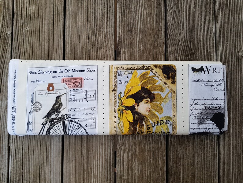 Op de afbeelding: Een opgerolde stof met vintage-stijl illustraties en tekst. Het ontwerp bevat een kolibrie op een fiets, bladmuziek en een vrouwenportret met de tekst "White, Black & Colors". De stof is cr&egrave;mekleurig met zwarte, gele en bruine accenten.