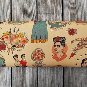 Op de afbeelding: Een beige stof met een herhalend patroon van Frida Kahlo ge&iuml;nspireerde illustraties. De illustraties omvatten een palet, bloemen, vogels en pijlen. De tekst "Mi Vida", "Viva", "Todo Para Ti", "Yo Te Quiero", "El Dolor El Placer Y La Muerte" is opgenomen in het patroon.