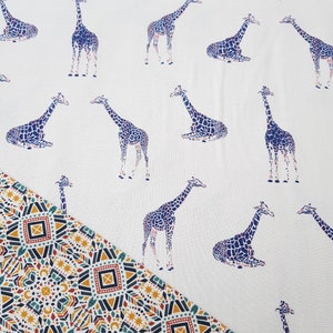 Peut inclure: Tissu blanc avec un motif répété de girafes violettes et roses. La moitié inférieure du tissu présente un motif géométrique coloré.