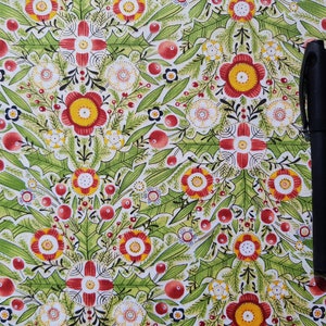 May include: A white fabric with a repeating pattern of red, yellow, and green flowers. The fabric has a black pen lying on top of it.