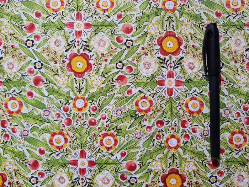 May include: A white fabric with a repeating pattern of red, yellow, and green flowers. The fabric has a black pen lying on top of it.