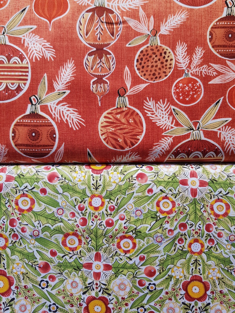 May include: Red fabric with a repeating pattern of stylized Christmas ornaments. The ornaments are in shades of orange, red, and brown. The background is a solid red. The fabric is folded in half, revealing a second fabric with a green and white floral pattern.