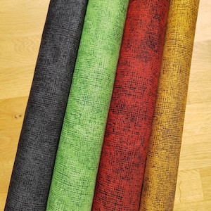 Könnte beinhalten: Vier Rollen Stoff mit verschiedenen Mustern. Der Stoff ist ein strukturiertes, gewebtes Material. Die Rollen sind schwarz, grün, rot und gold.