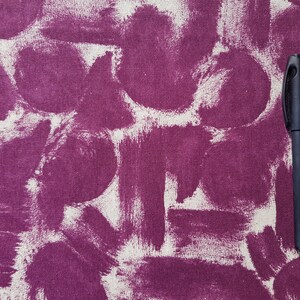 May include: A close-up of a purple fabric with white paint splatters and a black pen lying on top.