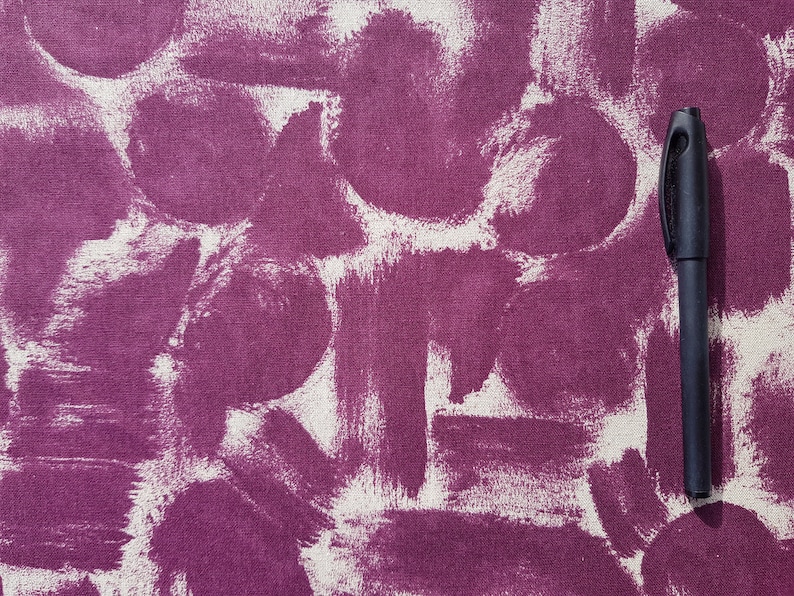 May include: A close-up of a purple fabric with white paint splatters and a black pen lying on top.