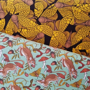 May include: A fabric with a repeating pattern of brown mice and red mushrooms on a light blue background. The fabric is folded over to reveal a second fabric with a repeating pattern of yellow moths on a black background.