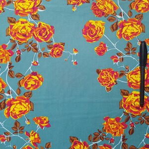 May include: Teal fabric with a floral pattern of orange and yellow roses. The fabric has a brown vine pattern.