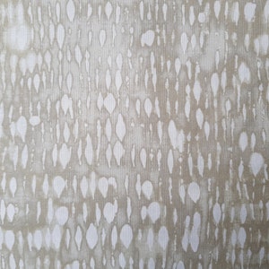 Può includere: Un tessuto beige con un motivo astratto bianco di piccole forme irregolari. Il motivo assomiglia a una serie di linee verticali con macchie bianche.