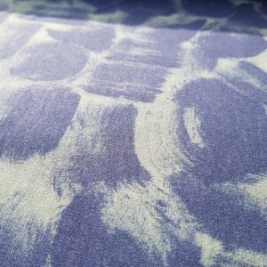 May include: A close-up of a blue fabric with a white tie-dye pattern. The fabric has a textured surface.