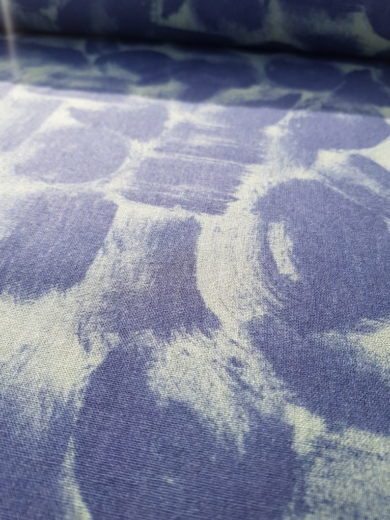 May include: A close-up of a blue fabric with a white tie-dye pattern. The fabric has a textured surface.