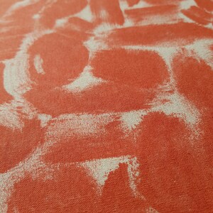 May include: Close-up of a textured fabric with a red background and white abstract shapes. The fabric has a linen-like texture.