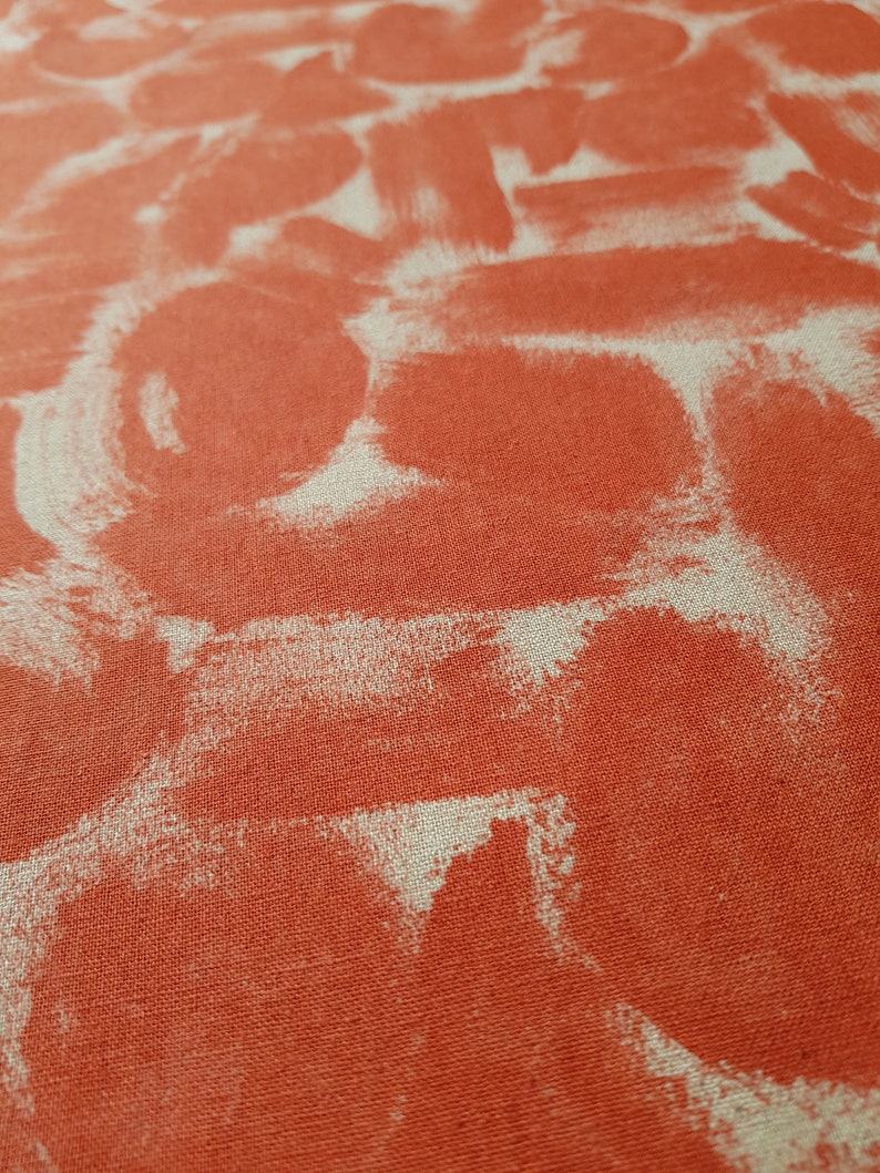 May include: Close-up of a textured fabric with a red background and white abstract shapes. The fabric has a linen-like texture.