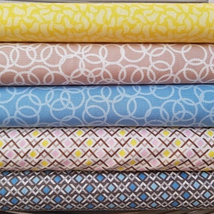 Könnte beinhalten: Vier Stoffmuster, die übereinander gestapelt sind. Das oberste Muster ist gelb mit einem weißen Muster. Das zweite Muster ist hellbraun mit einem weißen Muster. Das dritte Muster ist hellblau mit einem weißen Muster. Das unterste Muster ist braun mit einem weißen und blauen Muster.